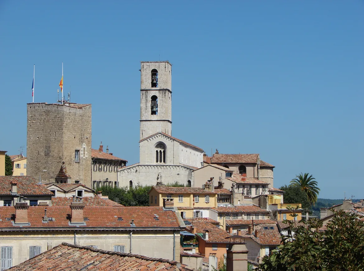 Grasse’s old town: a stone bell tower and a square keep above terracotta roofs and ochre houses under a clear blue sky.
